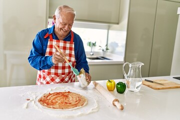Senior man smiling confident cooking pizza at kitchen