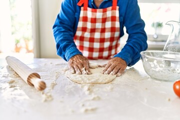 Obraz na płótnie Canvas Senior man cooking pizza dough with hands at kitchen
