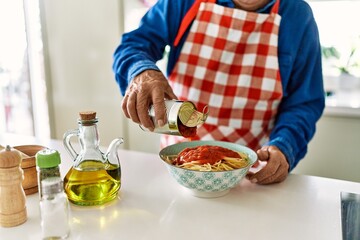 Senior man pouring tomato sauce on spaghetti at kitchen