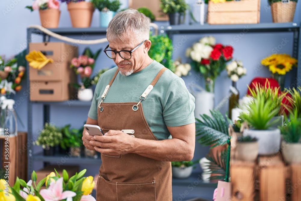 Wall mural Middle age grey-haired man florist using smartphone standing at flower shop