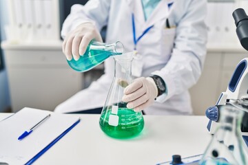 Senior man wearing scientist uniform pouring liquid at laboratory