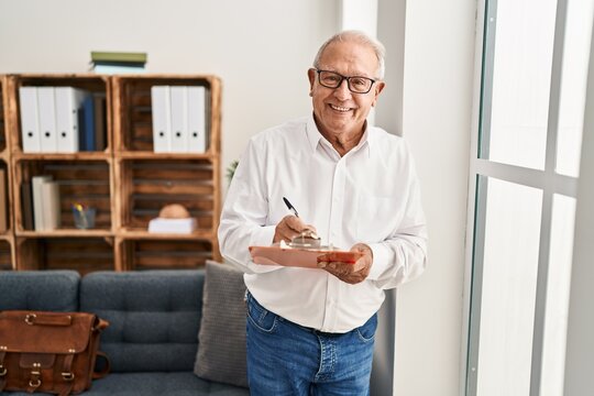 Senior man psychologist smiling confident writing on clipboard at psychology center