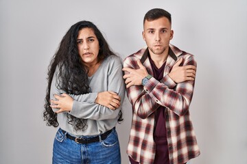 Young hispanic couple standing over white background shaking and freezing for winter cold with sad...