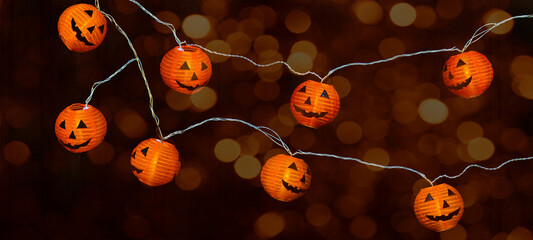 Happy HALLOWEEN party celebration background banner Panorama - Fairy lights, String of lights with funny orange glowing Halloween pumpkins jack o lantern and bokeh lights in the dark night