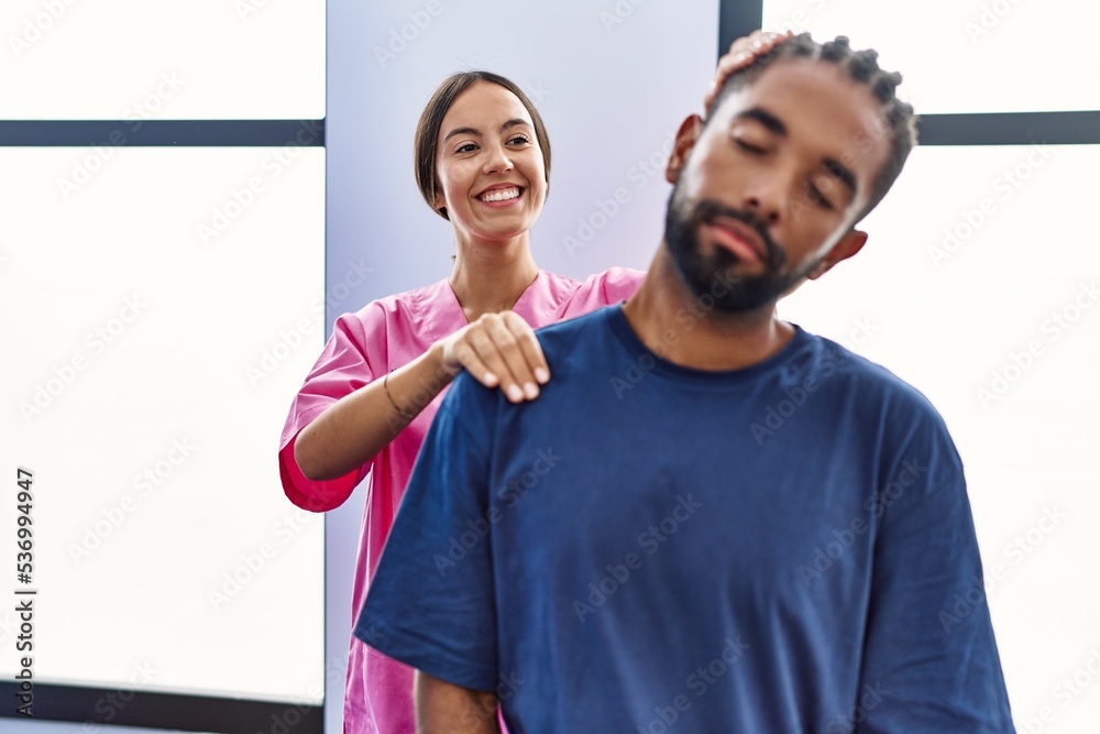 Wall mural Man and woman wearing physiotherapist uniform having rehab session stretching neck at physiotherpy clinic