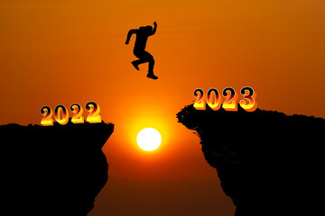 man silhouette jumping over a cliff, skipping 2022 into 2023 on the background of a new morning, happy New year concept.