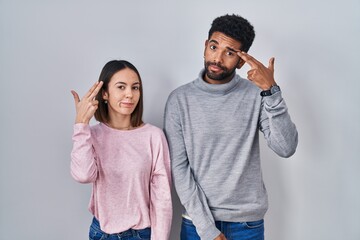 Naklejka premium Young hispanic couple standing together shooting and killing oneself pointing hand and fingers to head like gun, suicide gesture.