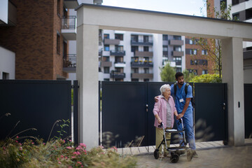 Caregiver walking with senior woman client in front of nurishing home.
