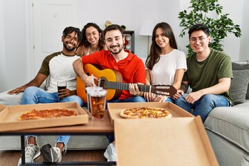 Group of young friends having party eating italian pizza and playing classical guitar at home.