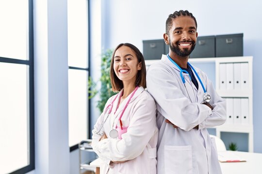 Man and woman wearing doctor uniform smiling confident standing with arms crossed gesture at clinic