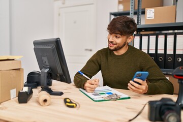 Young arab man ecommerce business worker writing on document using smartphone at office