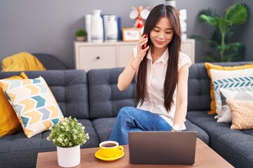 Young chinese woman talking on smartphone using laptop at home