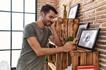 Young hispanic man smiling confident looking picture frame at home