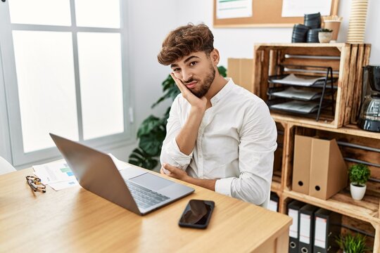 Young arab man working using computer laptop at the office thinking looking tired and bored with depression problems with crossed arms.