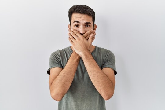 Young hispanic man with beard wearing casual t shirt over white background shocked covering mouth with hands for mistake. secret concept.