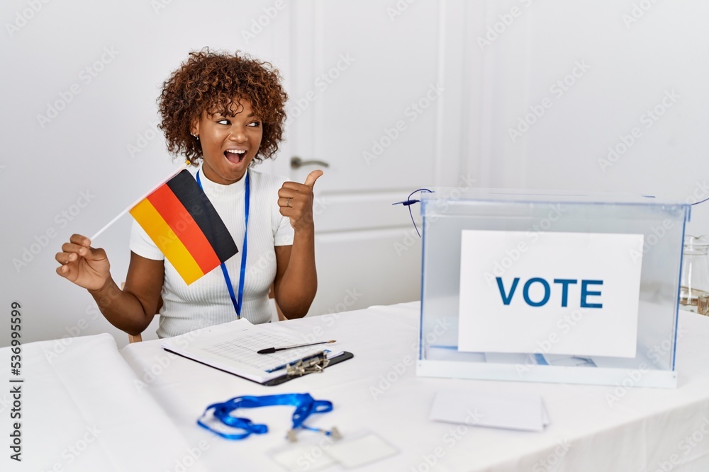 Sticker Young african american woman at political campaign election holding germany flag pointing thumb up to the side smiling happy with open mouth