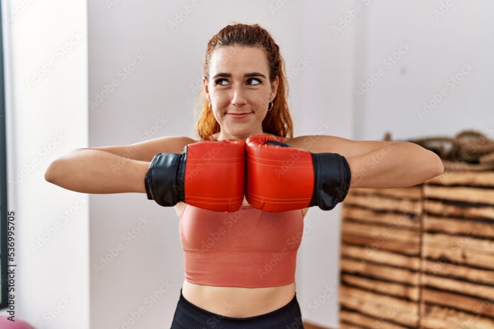 Poster young redhead woman using boxing gloves smiling looking to the side and staring away thinking.