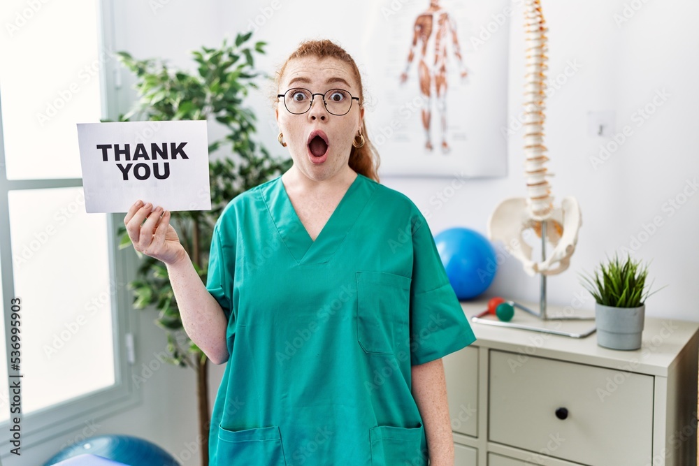 Canvas Prints young redhead physiotherapist woman working at pain recovery clinic holding thank you banner scared 