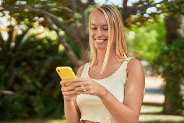 Young blonde woman smiling confident using smartphone at park