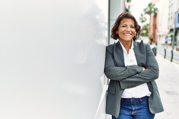 Middle age latin businesswoman smiling happy standing with arms crossed gesture at the city.