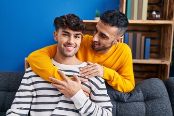 Two man couple hugging each other sitting on sofa at home