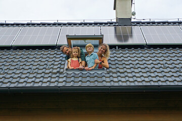 Happy family leaning out from skylight window in their new house with solar panels on the roof....