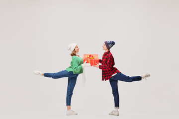 Emotional young people, ballet dancers in warm clothes in action, motion with bright festive gift boxes on gray background. Holidays, happiness concept