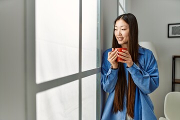 Fototapeta premium Young chinese girl drinking coffee standing at home.