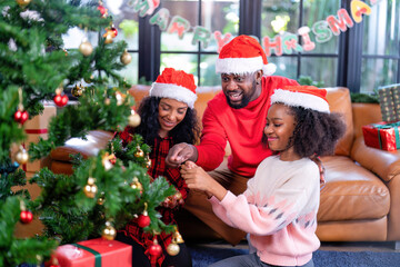 American family happy laughing celebrate christmas eve sitting at leather brown sofa in leaving room decoration with green christmas tree and lighting, father give surprise gift box to daughter