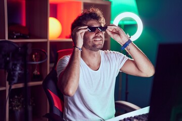 Young hispanic man streamer smiling confidetn wearing thug life glasses at music studio