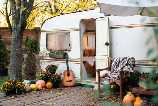Mobile home van with terrace at sunset in autumn, mobile home, orange fallen leaves. autumn decor, pumpkins