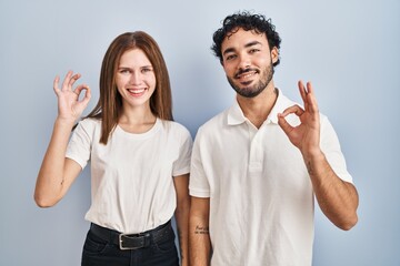 Young couple wearing casual clothes standing together smiling positive doing ok sign with hand and fingers. successful expression.