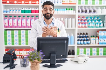 Hispanic man with beard working at pharmacy drugstore smiling with hands on chest with closed eyes...