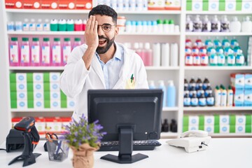 Hispanic man with beard working at pharmacy drugstore covering one eye with hand, confident smile on face and surprise emotion.