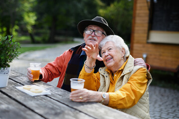 Happy senior couple in forest buffet resting after walk, having beer and admiring nature.