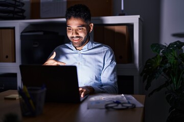 Hispanic man with beard working at the office with laptop at night pointing finger to one self smiling happy and proud