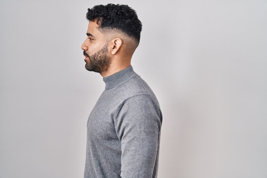 Hispanic man with beard standing over white background looking to side, relax profile pose with natural face and confident smile.