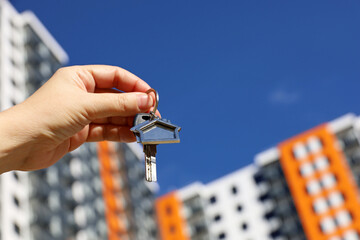 Female hand with home keys on background of new building. Real estate agent, byung apartment or renting property