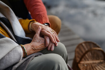 Close up of senior couple holding each other hand and sitting near lake.