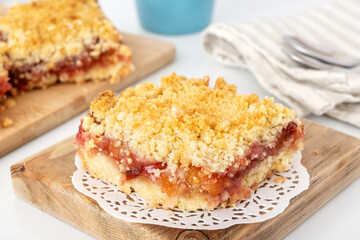 Portion of crumbly shortbread pie with plum and apple jam on wooden board. Dessert with fruit and streusel.