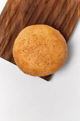 white bun with sesame seeds on the edge of a kitchen board on a white background