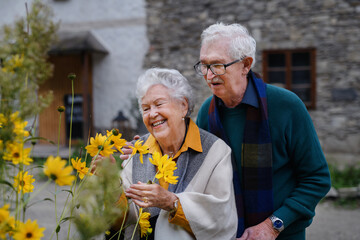 Happy senior couple at autumn city walk, posing with flowers.