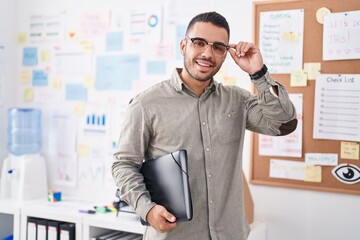 Young hispanic man business worker smiling confident holding binder at office