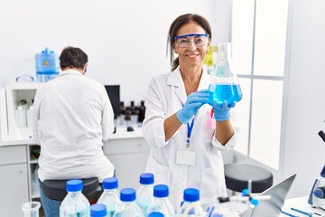 Fototapeta premium Middle age man and woman partners wearing scientist uniform holding test tube at laboratory