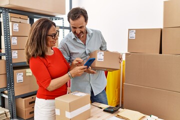 Middle age man and woman business partners using smartphone holding package at storehouse