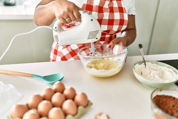 Obraz na płótnie Canvas Hispanic brunette woman preparing cake with electric whisk at the kitchen