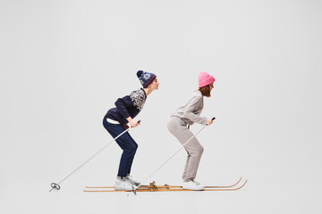 Winter stroll. Two funny retro skiers in warm winter casual wear skiing isolated on grey background. Retro, vintage, sport, holidays, hobbies concept