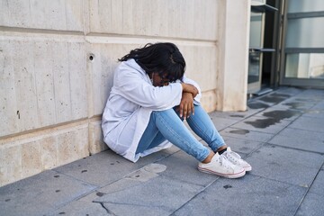 Young beautiful latin woman doctor stressed sitting on floor at hospital