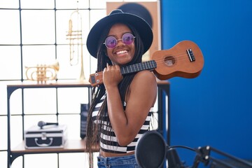 Fototapeta na wymiar African american woman musician smiling confident holding ukulele at music studio