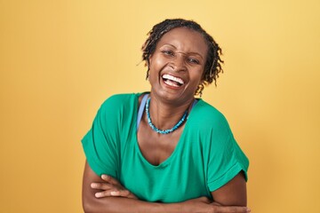 African woman with dreadlocks standing over yellow background smiling and laughing hard out loud...